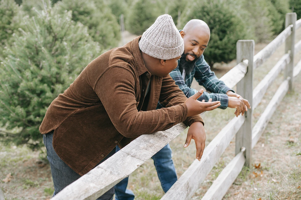 A father and son having a conversation at a tree farm, leaning over a rustic wooden fence