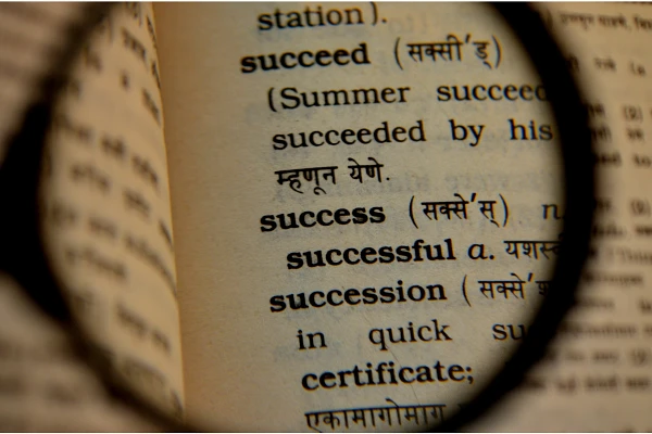 A magnifying glass is focusing on the word "success" and its definition in a bilingual dictionary.